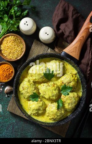 Fleischbällchen mit Bulgur in saurer Sahne und Kurkuma-Sauce in einer Pfanne auf einer dunklen Steinplatte. Draufsicht flach legen Hintergrund. Stockfoto