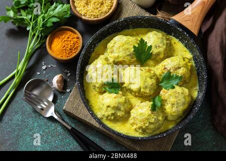 Fleischbällchen mit Bulgur in saurer Sahne und Kurkuma-Sauce in einer Pfanne auf einer dunklen Steinplatte. Stockfoto