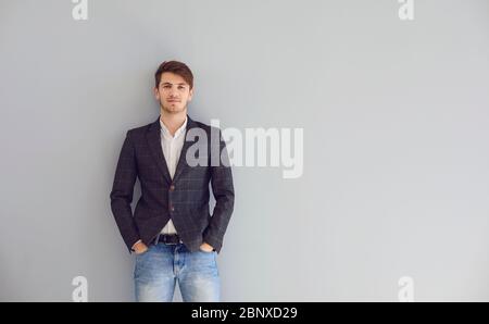 Junger ruhiger, selbstbewusster Mann in einer lässigen Jacke stehend mit Blick auf grauen Hintergrund. Geschäftsmann freiberuflich Student Designer Manager Arbeiter Architekt Stockfoto
