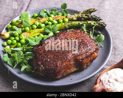 Gebratenes Rindersteak, Hammelfleisch mit Spargelerbsen auf einem Teller, weiße Sauce Stockfoto