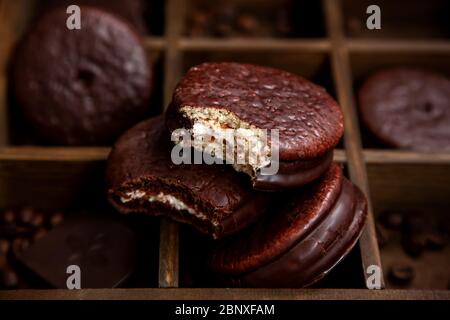 Ein paar süße Choco Pie Desserts auf einem hölzernen Hintergrund unter verstreuten Kaffeebohnen.Schokolade und klassisches Dessert Choco Pie Stockfoto