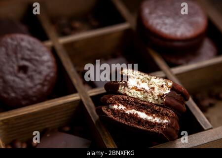 Ein paar süße Choco Pie Desserts auf einem hölzernen Hintergrund unter verstreuten Kaffeebohnen.Schokolade und klassisches Dessert Choco Pie Stockfoto