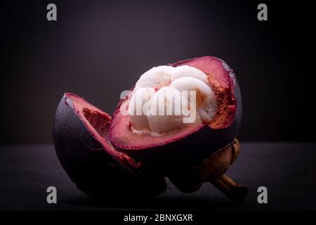 Hälften einer purpurroten exotischen Mangostan-Frucht, die das weiße Fleisch in Knospen zeigt und die dicke, magentafarbene, schwammartige äußere Schale offenbart. Stockfoto