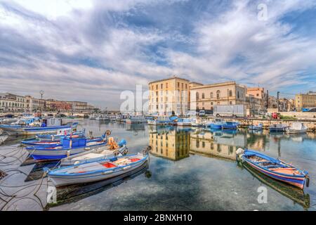 Syrakus Sizilien/ Italien -April 11 2020: Die Fischerboote liegen im Kanal des Ortigia-Anlegesteg und der Palast spiegelt sich in seinen Gewässern wider Stockfoto