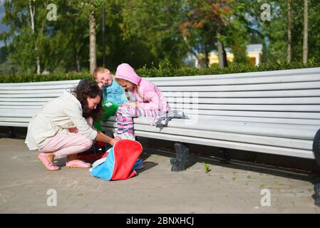 Mutter im Park auf der Bank stellt Kinder auf seine Füße Rollschuhe in St. Petersburg Stockfoto