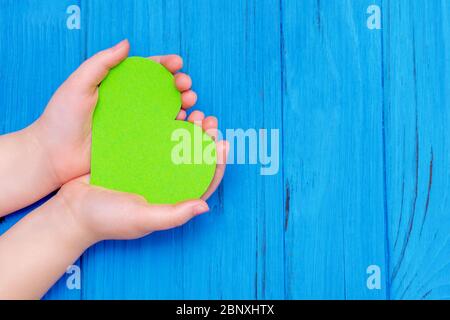 Draufsicht des grünen Herzens in Händen des Kindes auf Holz blauen Hintergrund. Kopierbereich. Konzept des Umweltschutzes und des Erdtages. Stockfoto