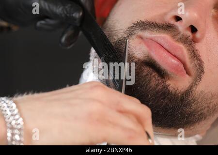 Haarschnitt eines Männerbarts in einem Friseurladen. Professioneller Meister-Barbier rasiert den Bart des Kunden mit einer Schere. Barbier Men. Werbung und Friseur sh Stockfoto