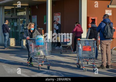 Tuscany, Italy 04/10/20: Überfüllte und chaotische Szene vor einem Lebensmittelgeschäft: Eine Gruppe italienischer weißer Menschen mit Coronavirus-Masken, die eintreten und austreten Stockfoto