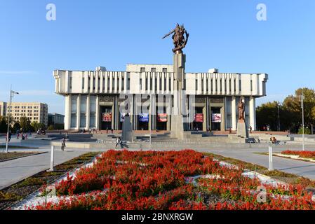 Kirgisische Nationalphilharmonie in Bischkek, Kirgisistan, benannt zu Ehren von Toktogul Satylganov und in der Sowjetzeit im brutalistischen Stil erbaut. Rote Blumen Stockfoto