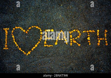 Ich liebe die Erde, Textnachricht über Respekt für unseren Planeten Erde. Gelbe, orangefarbene Felsen bilden Buchstaben und Worte auf einem schönen schwarzen Sandgrund. Symbol Stockfoto