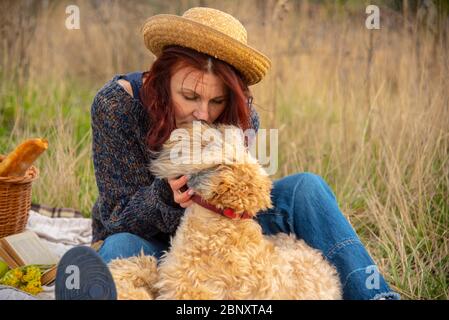 Porträt einer 40-jährigen Frau in einem Strohhut mit einem Hund auf einem Picknick. Stockfoto