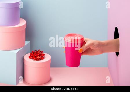 Die Hand der Frau hält eine rosa Tasse Kaffee aus Papier auf blauem und rosa Hintergrund Stockfoto