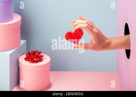 Die Hand der Frau hält ein rotes Papierherz auf blauem und rosa Hintergrund Stockfoto