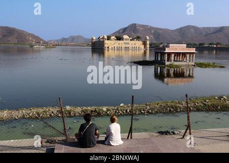 Ein paar westliche Touristen, die einen berühmten Palast am See in Jaipur, Rajasthan, Indien, erwägen. Stockfoto