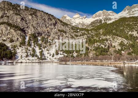 Winterlandschaft in der Lagune des Kurortes Panticosa mit den Bergen im Hintergrund mit Schnee aus den Pyrenäen, Huesca, Aragon, Spanien. Stockfoto