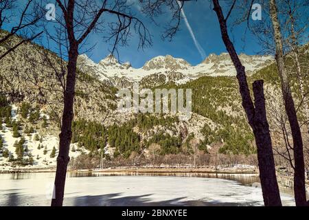 Winterlandschaft in der Lagune des Kurortes Panticosa mit den Bergen im Hintergrund mit Schnee aus den Pyrenäen, Huesca, Aragon, Spanien. Stockfoto