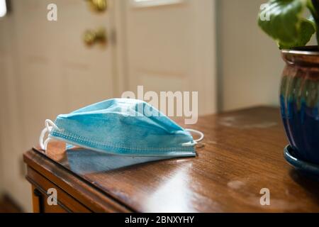 Maske auf Tisch mit Blick auf Tür. Mit Maske als Schutz vor Coronavirus, um die Kurve zu glätten Stockfoto