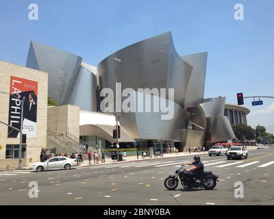 Walt Disney Concert Hall Haupteingang mit blauem Himmel Hintergrund. Autos und ein Motorradfahrer im Vordergrund. Frank Gehry entwarf Musikhalle mit markanten Stockfoto