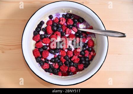 Haferflocken Haferbrei mit gefrorenen Beeren Himbeeren und Heidelbeeren in einem Weiße Schüssel mit einem Löffel auf einem Holztisch Stockfoto