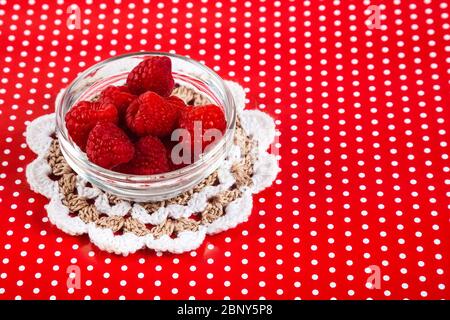 Reife Himbeeren in einer Glasschale. Roter Hintergrund mit weißen Flecken. Stockfoto