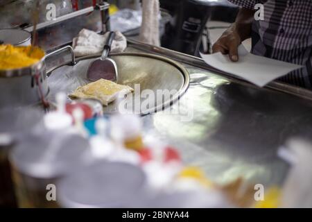 Prozess für die Herstellung von leckeren traditionellen Thai-Pfannkuchen auf einer Straße Theke. Männliche Hände braten einen Pfannkuchen in Öl. Lokale Spezialität Stockfoto
