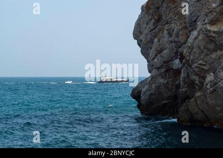 Malerischer Felsen vor der Küste des Meeres. Weißes Boot auf den Wellen Stockfoto