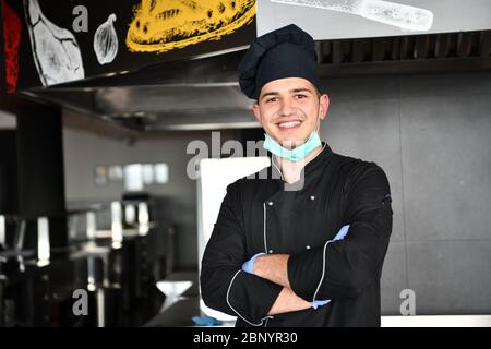 Koch tragen Gesicht schützende medizinische Maske für den Schutz vor Corona-Virus-Krankheit mit Teller mit authentischen Sandwich im professionellen Restaurant KI Stockfoto