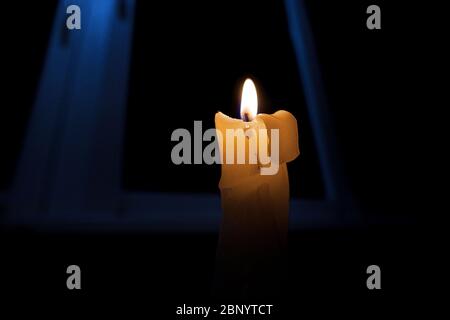 Brennende Kerze in völliger Dunkelheit, vor dem Hintergrund des Fensters. Stockfoto