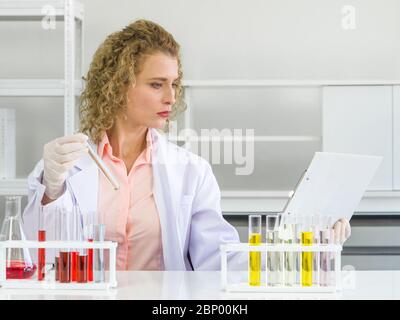 Junge blonde Wissenschaftler vergleichen die Ergebnisse neuer chemischer Forschung mit experimentellen Diagrammen auf dem Clipboard. Arbeitsatmosphäre in chemischer l Stockfoto