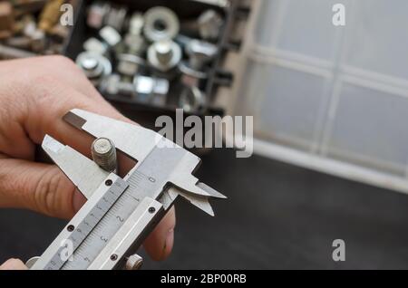 Eine männliche Hand mit einem Bremssattel misst den Durchmesser einer Schraube. Die Wahl des richtigen Metallverbinders. Verwendung von manuellen Messgeräten. Fokus in der Stirn Stockfoto