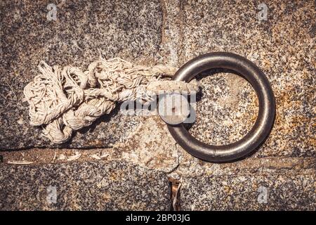 Stahlring und Festmacherlinien in einem Seehafen. Helles Hanfseil auf dem Boden. Stockfoto