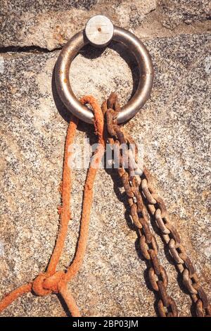 Stahlring und Festmacherlinien in einem Seehafen. Rostige Eisenkette und orangefarbenes Hanfseil. Stockfoto