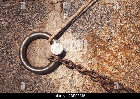 Stahlring und Festmacherlinien in einem Seehafen. Rostige Eisenkette und Hanfseil auf dem Betonboden. Stockfoto