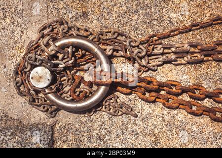 Rostiger Stahlring und Festmacherlinien in einem Seehafen. Rostige Eisenkette auf dem Boden. Stockfoto