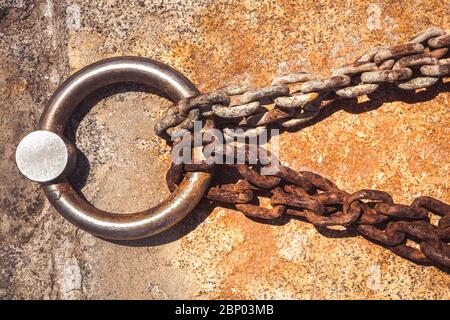 Rostiger Stahlring und Festmacherlinien in einem Seehafen. Rostige Eisenkette auf dem Betonboden. Stockfoto