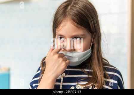 Kleinkind Mädchen mit medizinischen Maske auf Gesicht. Covid19 Corona Virus Ausbruch. Mädchen berührt Gesicht schmutzige Hände, es ist nicht sicher. Trauriges Mädchen ist es leid, bei h zu sitzen Stockfoto
