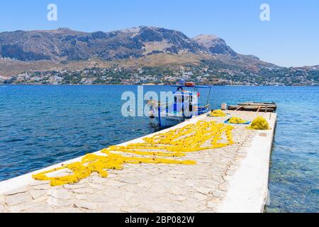 Fischerboot und gelbe Netze zum Trocknen auf dem Steg der kleinen Hafenstadt Telendos Island, Kalymnos, Dodekanes, Griechenland Stockfoto