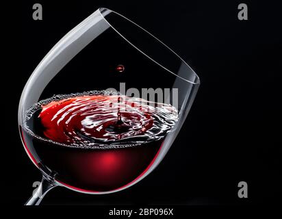 Rotwein in einem Weinglas isoliert auf schwarzem Grund. Tropfen fällt auf die Oberfläche und erzeugt Wellen. Stockfoto