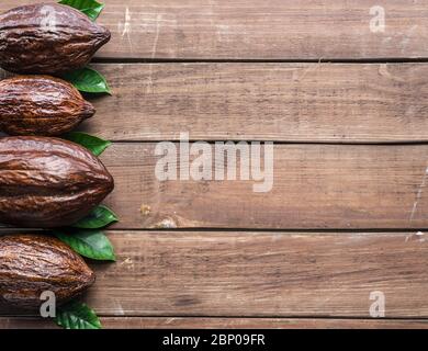 Kakaoschote und Kakaoblätter als Teil des Rahmens auf Holzhintergrund angeordnet. Stockfoto