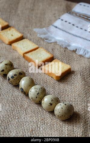 Quadratische Croutons und rohe Wachteleier auf Burlap. Eine Reihe von Croutons und Wachteleiern. Zutaten für ein traditionelles Gericht. Ansicht von oben in einem Winkel. Selektiv f Stockfoto