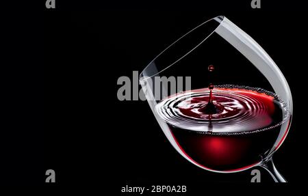 Rotwein in einem Weinglas isoliert auf schwarzem Grund. Tropfen fällt auf die Oberfläche und erzeugt Wellen. Stockfoto