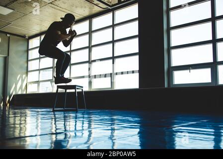 Sportmann springt auf einer speziellen Plattform in der Turnhalle gegenüber dem Fenster. Silhouette erschossen Stockfoto