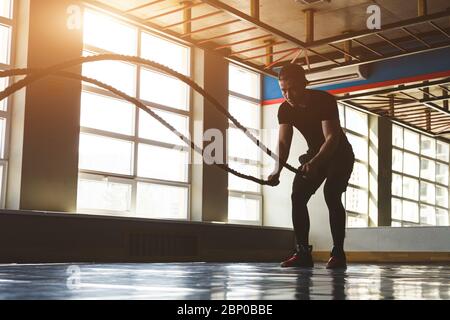 Trainieren Sie mit Seilen. Der Sportler trainiert im Fitnessstudio gegenüber großen Panoramafenstern. Stockfoto