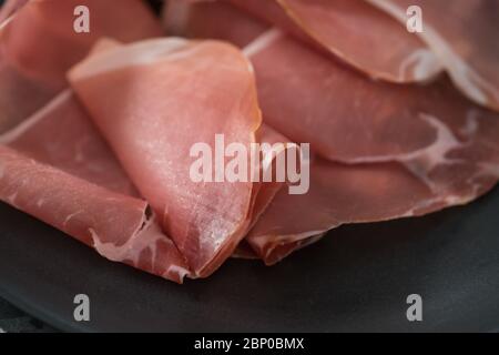 Dünne italienische Prosciutto-Scheiben auf schwarzem Teller auf conctere Hintergrund Nahaufnahme Stockfoto