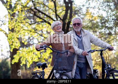 Altes Paar mit Fahrrädern, die im Park spazieren gehen Stockfoto