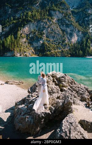 Die Braut und der Bräutigam stehen auf Steinen mit Blick auf den Lago di Prags in Italien. Hochzeitstag in Europa, am Pragsersee. Liebevolle Brautpaare Stockfoto
