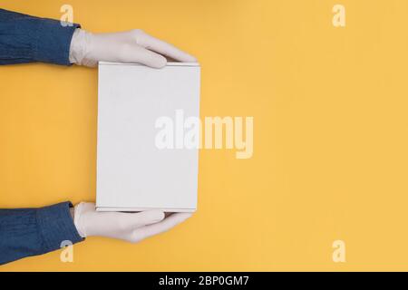 Kurierhände in medizinischen Handschuhen halten einen Karton auf gelbem Hintergrund Stockfoto