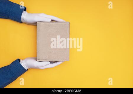 Kurierhände in medizinischen Handschuhen halten einen Karton auf gelbem Hintergrund Stockfoto