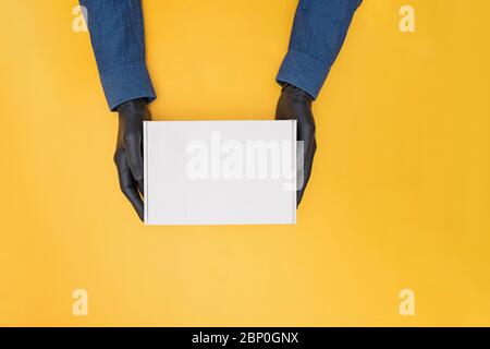 Kurierhände in medizinischen Handschuhen halten einen Karton auf gelbem Hintergrund Stockfoto