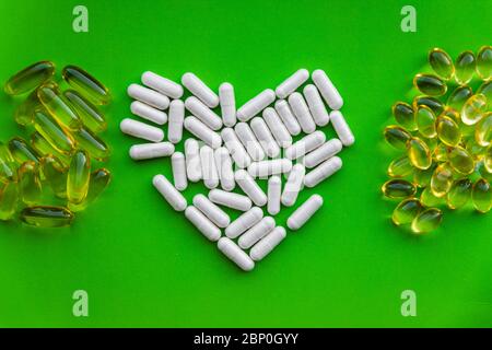 Herzform von weißen Vitaminpräparaten mit Stapel von gelben Gelee-Pillen, liebevolle Gesundheit Diätkapsel auf hellgrünem Hintergrund mit Kopieraum Stockfoto
